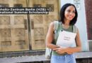 A smiling student holding a scholarship application form outside a university building – Helmholtz-Zentrum Berlin International Scholarship 2025.